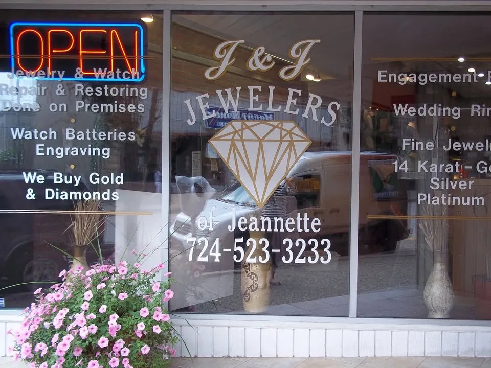 The shop's front window, lettered with J & J Jewelers of Jeannette over a gold diamond, the phone number and the work done on the premises