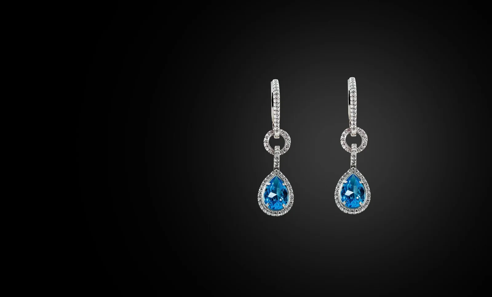 Diamond drop earrings set with pear-shaped blue stones, on black