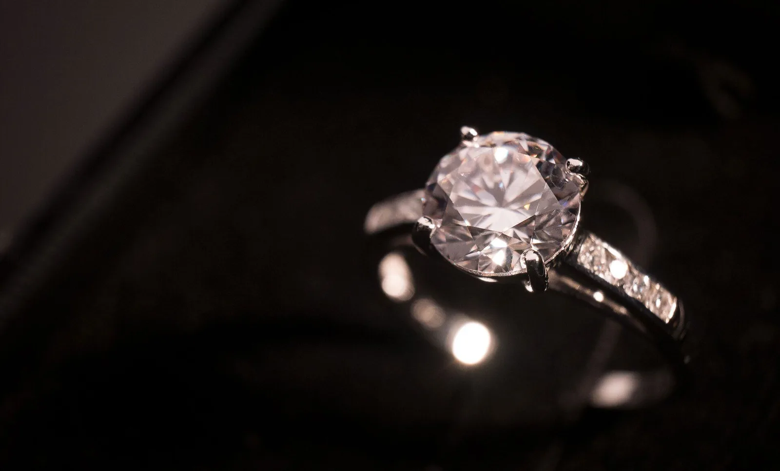 A round diamond solitaire with small diamonds down its band, on dark velvet