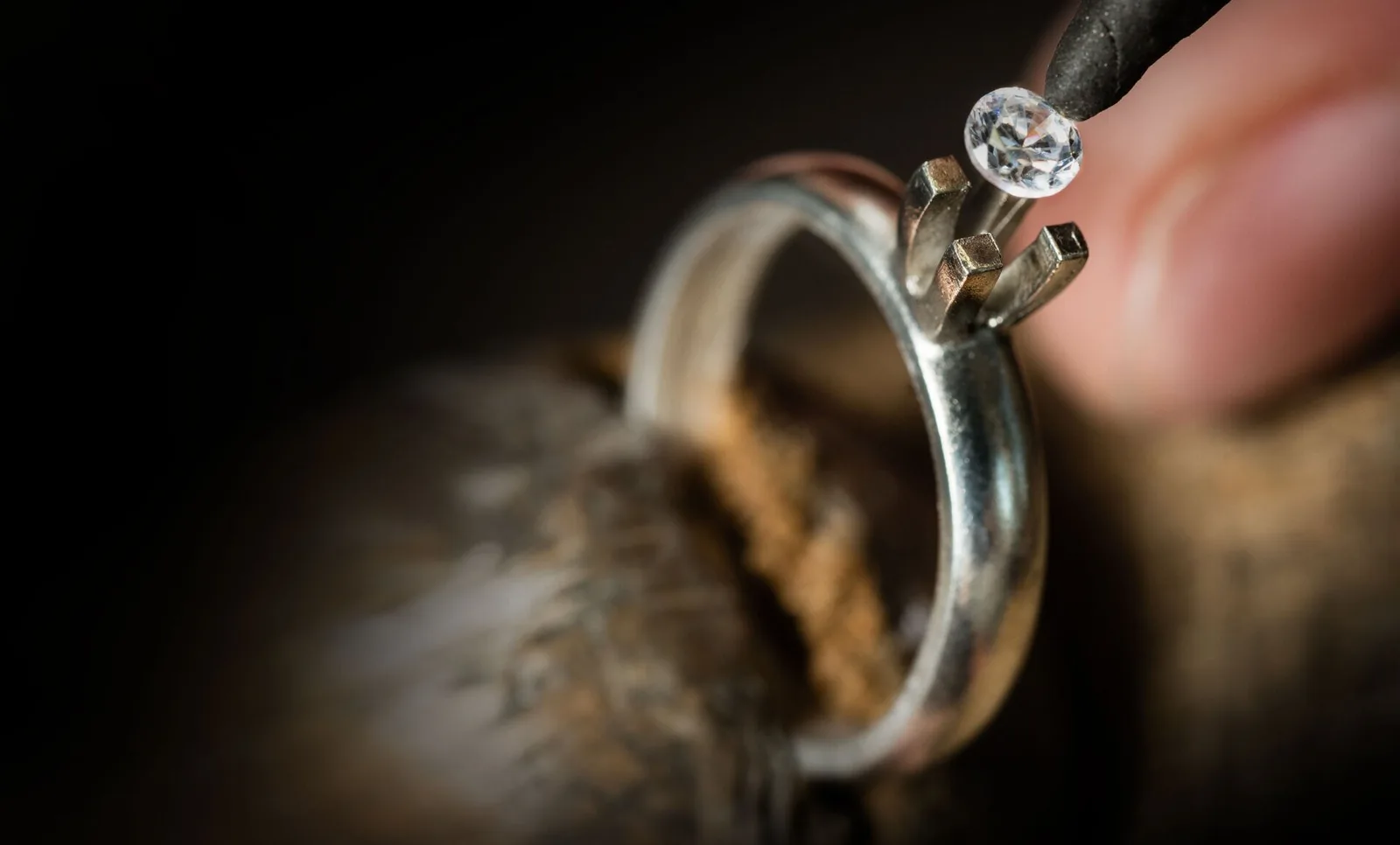 A diamond held in tweezers over the open prongs of a ring